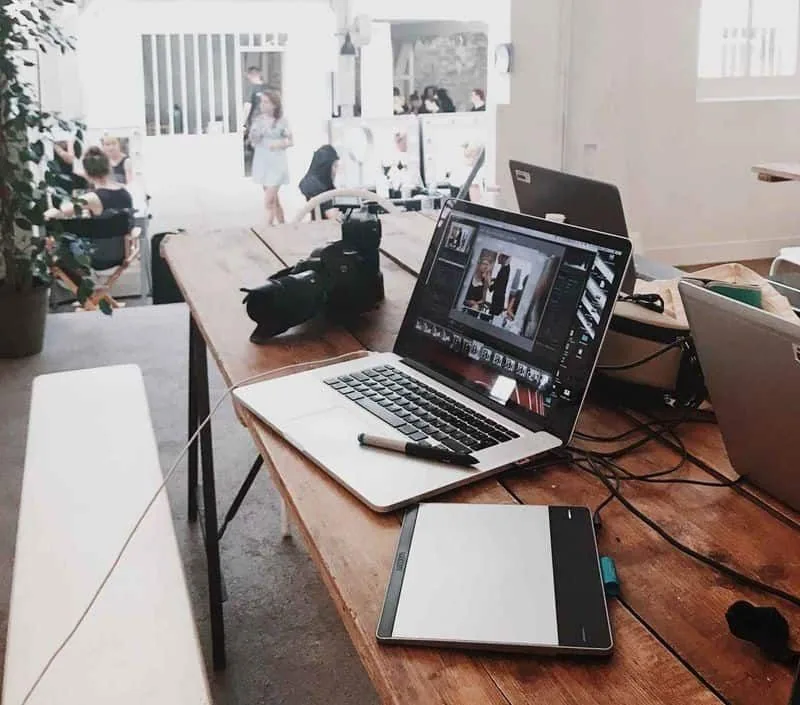 Creative studio desk with a laptop, camera and drawing tablet, the team working behind